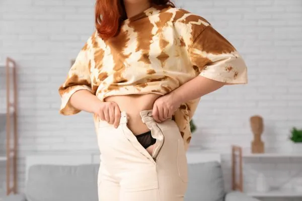 Image of woman trying to do her trousers up after pregnancy weight gain Merry Hill